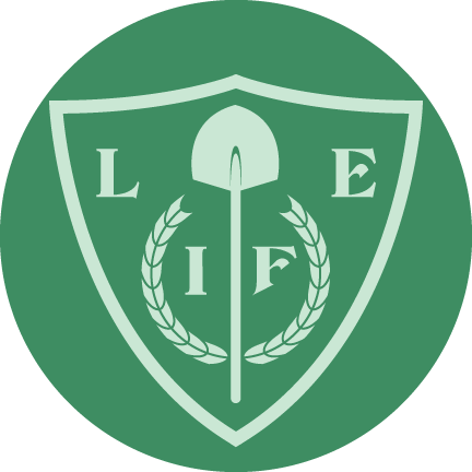 A shield with the word "Life," a shovel, and wreaths inside it, all on a green background.